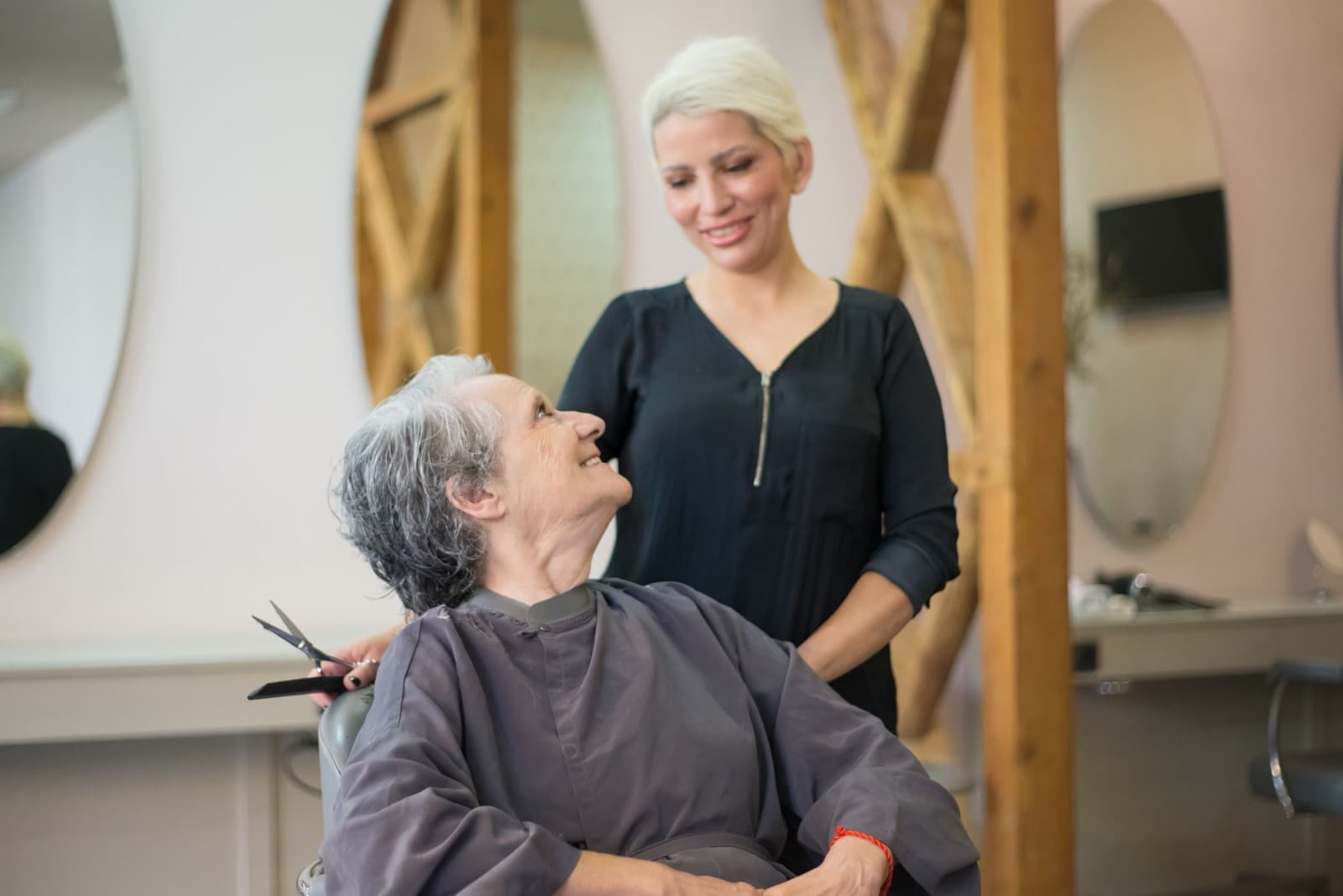Friseurin und ältere Kundin lächeln sich während des Haarschnitts an